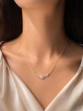A delicate gold necklace with a small floral cluster pendant, worn by a model in a satin cream top.