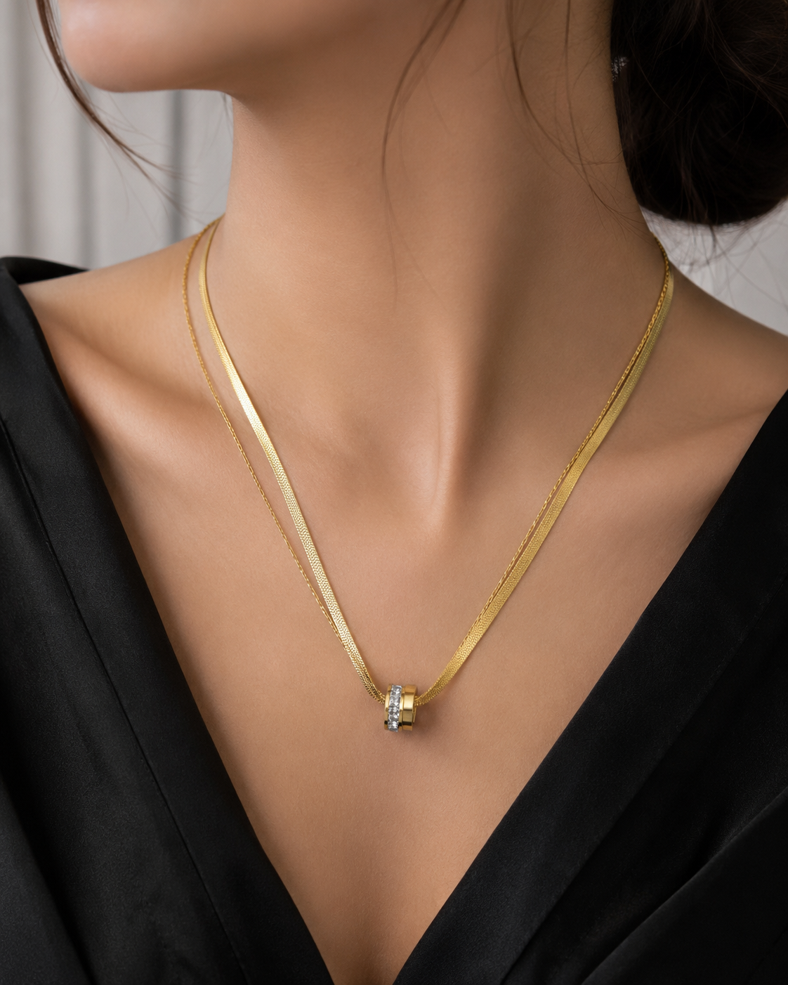 A close-up of a model's neck and upper chest wearing a delicate gold chain necklace with a small central pendant featuring a clear gemstone and a tiny gold accent.
